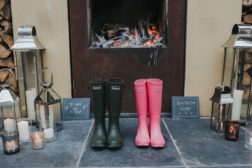 bride and groom wellington boots in front of the fire on the terrace with 'from this day forward' and 'to have and to hold' signs behind