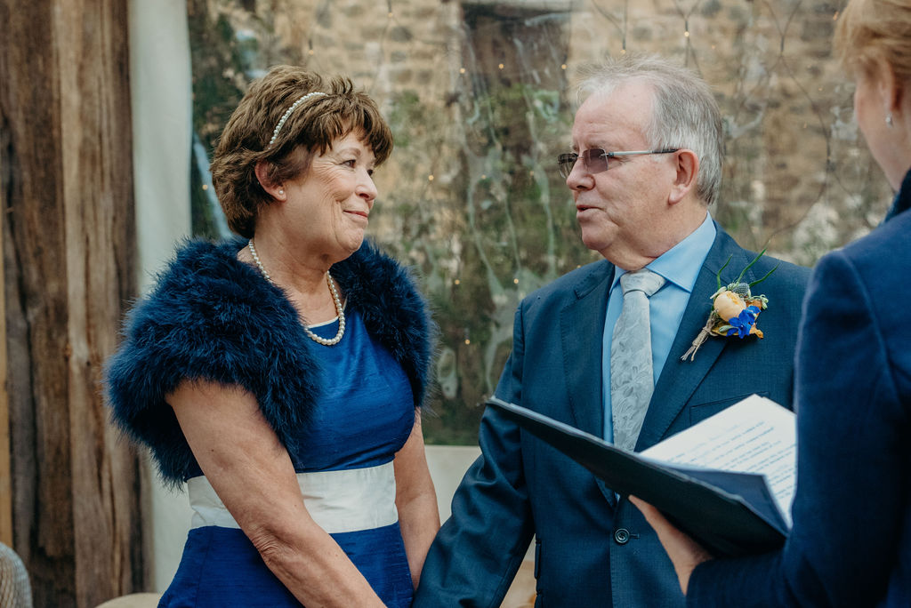 older bride and groom looking at each other during wedding ceremony bride wearing navy blue dress and navy feather shrug groom wearing navy suit 