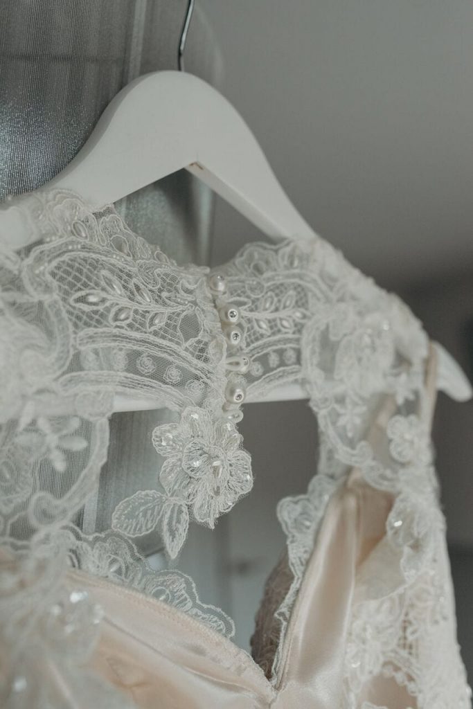 detailed image of lace dress on hanger, showing the cutout back and pearl buttons.