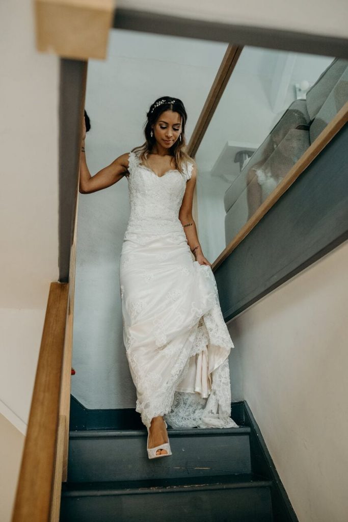 bride walking down the stairs in lace dress looking down and showing her matching lace shoes.