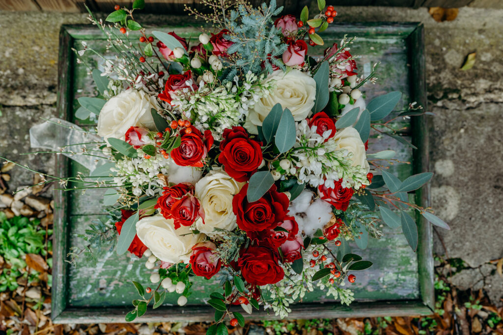 overhead view of a large white and red rose wedding bouquet stood on a vintage green painted board