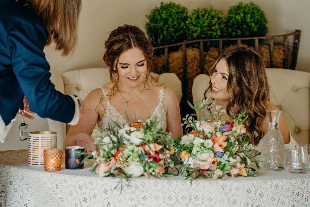 two brides smiling signing wedding register with flower bouquets