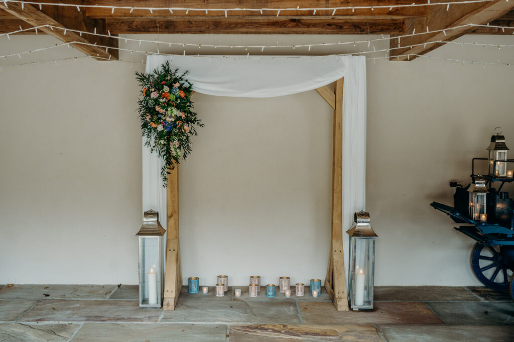 wedding ceremony backdrop wooden arch with flower spray lanterns and tealights