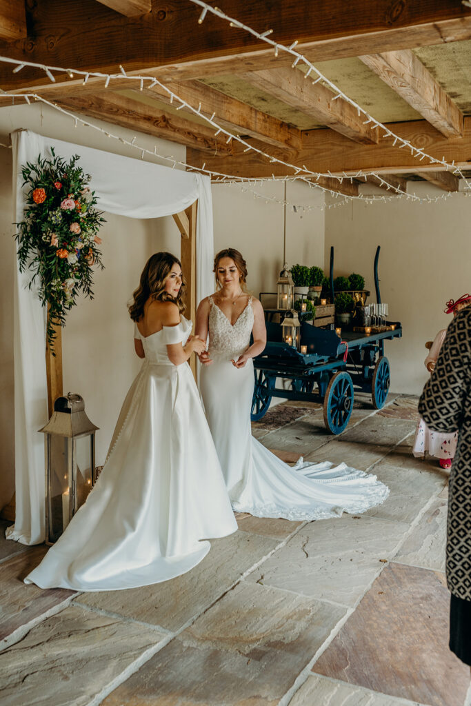 two brides at elopement ceremony in rustic wedding barn in white bridal gowns 