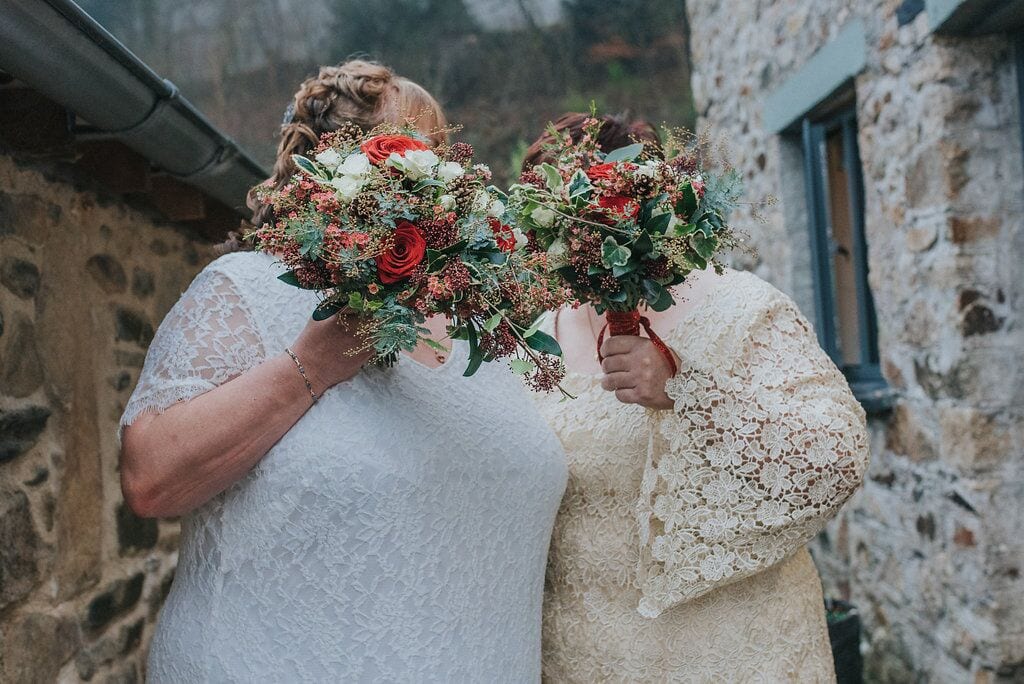 two brides hiding behind their red bouquets 