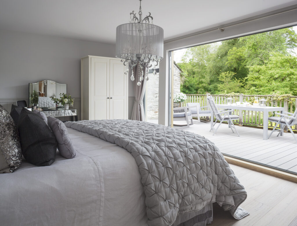 honeymoon suite decorated in silver greys with quilted eiderdown and bifold doors open to a deck with green trees in the backdrop