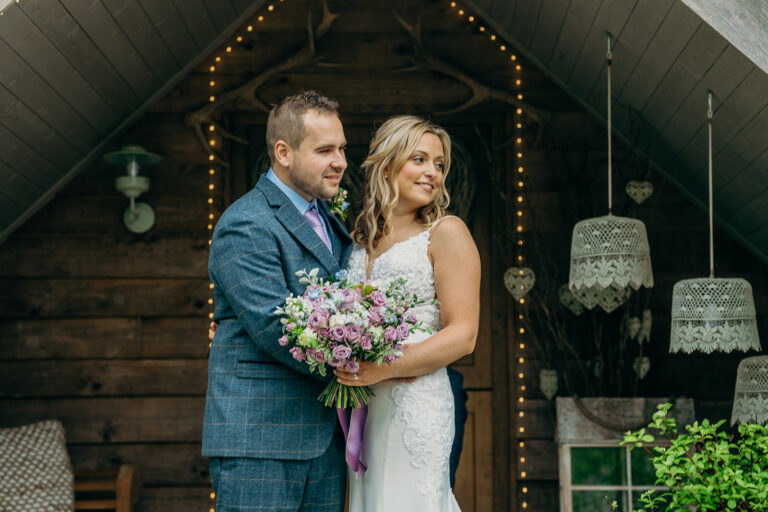 bride and groom with wedding bouquet in front of rustic backdrop