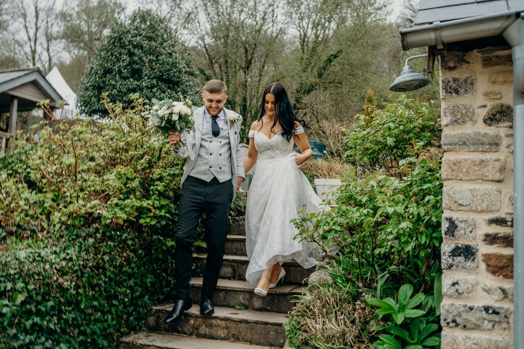 bride and groom walking down wood steps lined with plants groom carrying bouquet