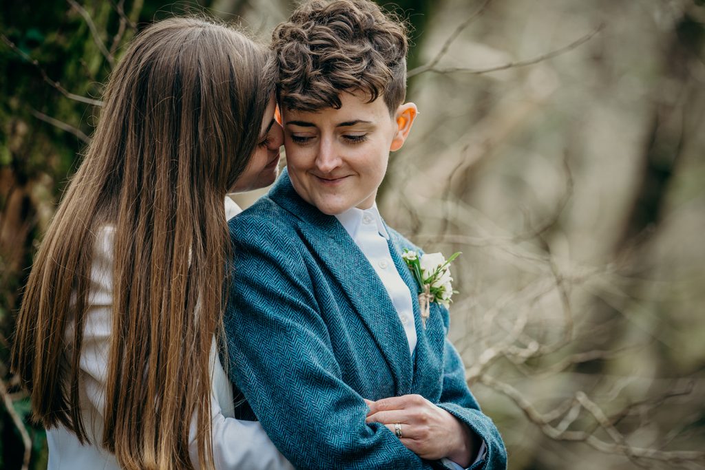 close up of two brides in suits one with long hair in Devon woodland