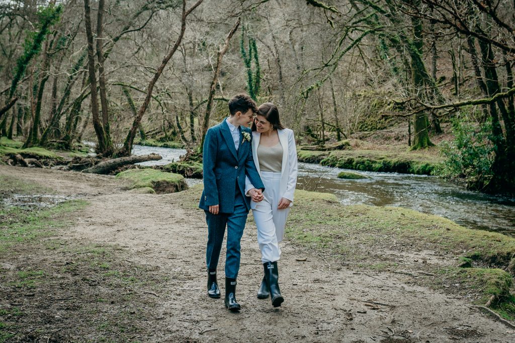 two brides in suits holding hands walking by the bank of a river