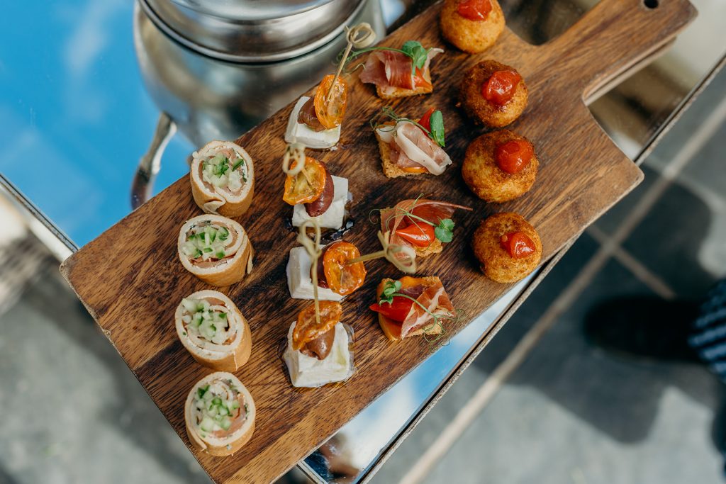 close up of a wooden board with 4 rows of canapes resting on a mirrored table top