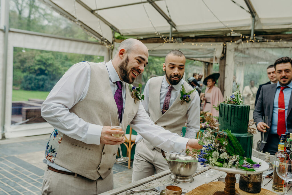 two grooms looking at a dark green iced wedding cake