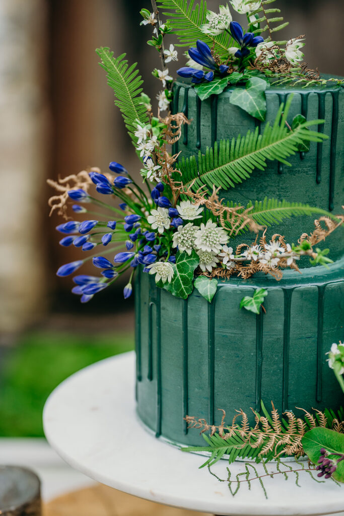 dark green iced drip cake on a marble cake stand decorated with ferns and flowers