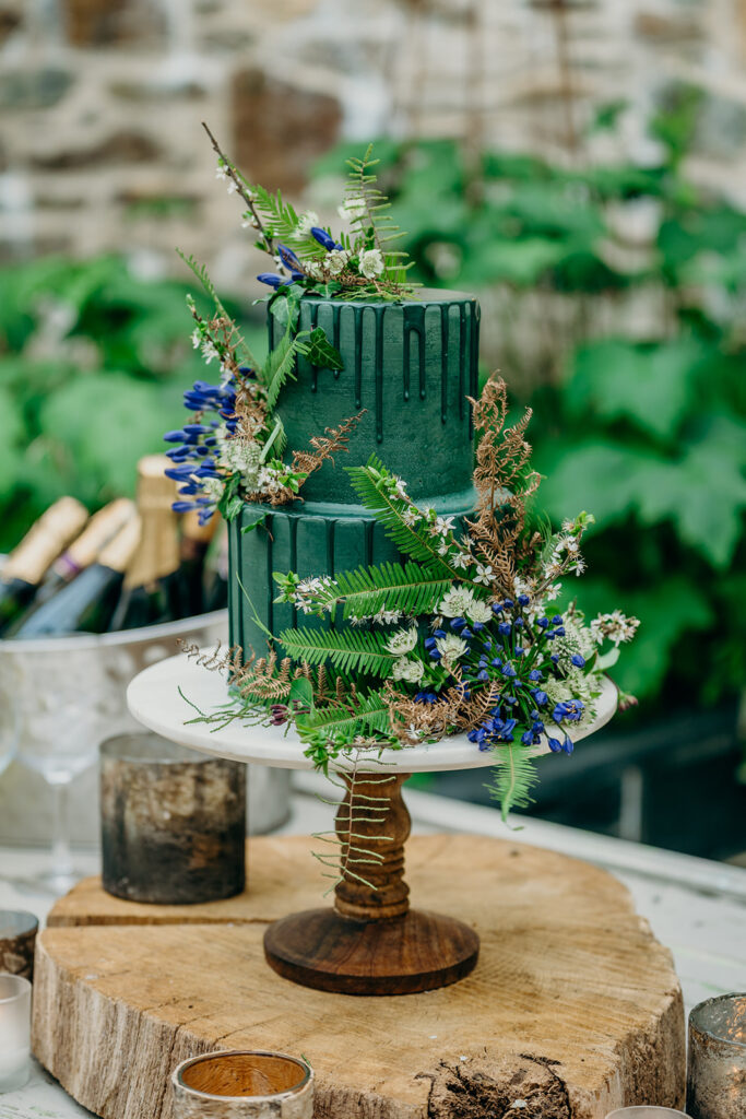 dark green iced drip cake on a log slice decorated with ferns