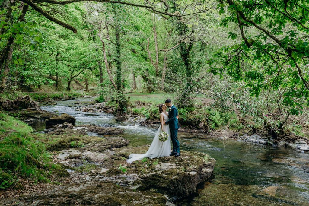 wedding couple stood on the bank of a dartmoor river under green tree canopy