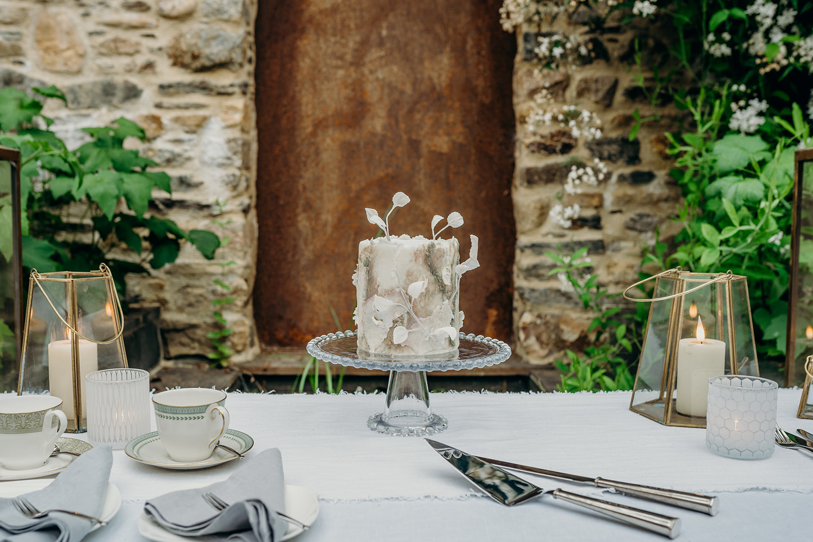wedding cake table with textured mini wedding cake in front of rust water feature and stone walls