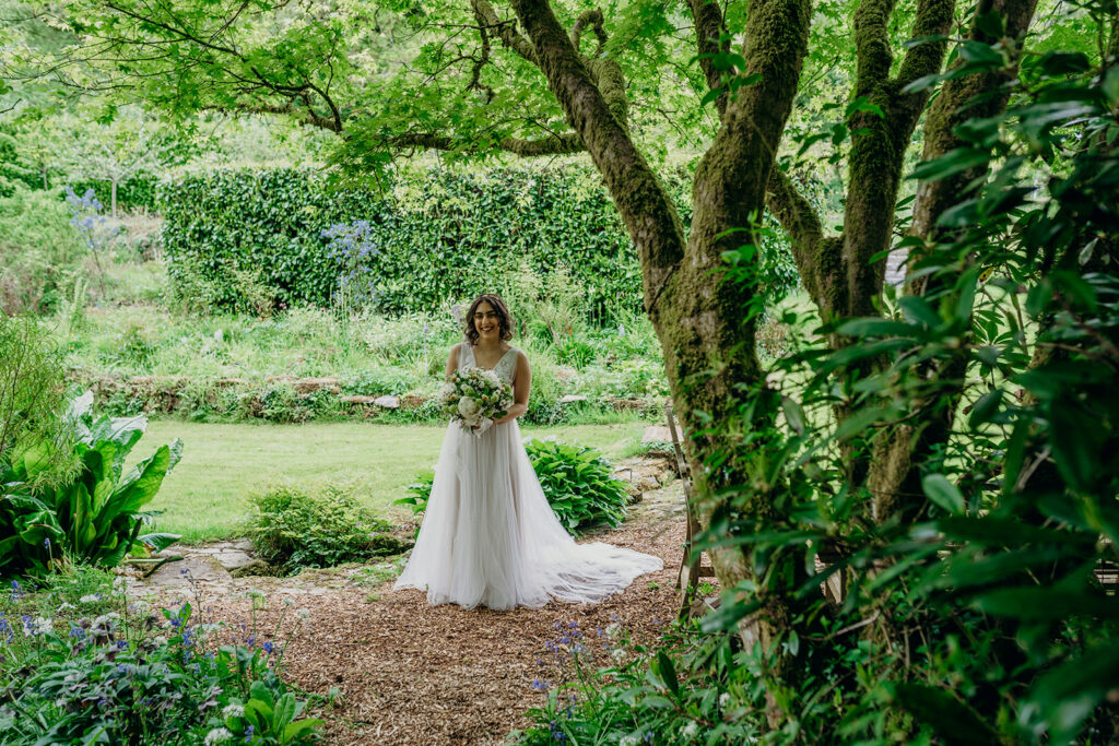 bride walking alone in green gardens to wedding ceremony 
