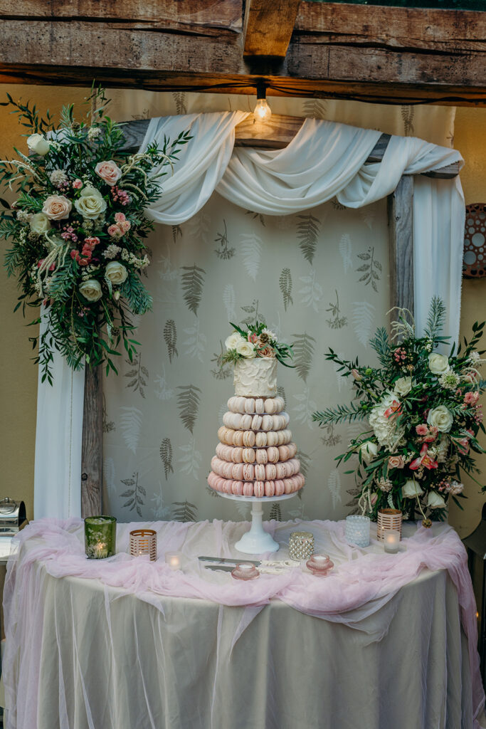 pink ombre macaron tower topped with buttercream mini wedding cake in front of fabric draped wooden arch dressed with pink and white flowers