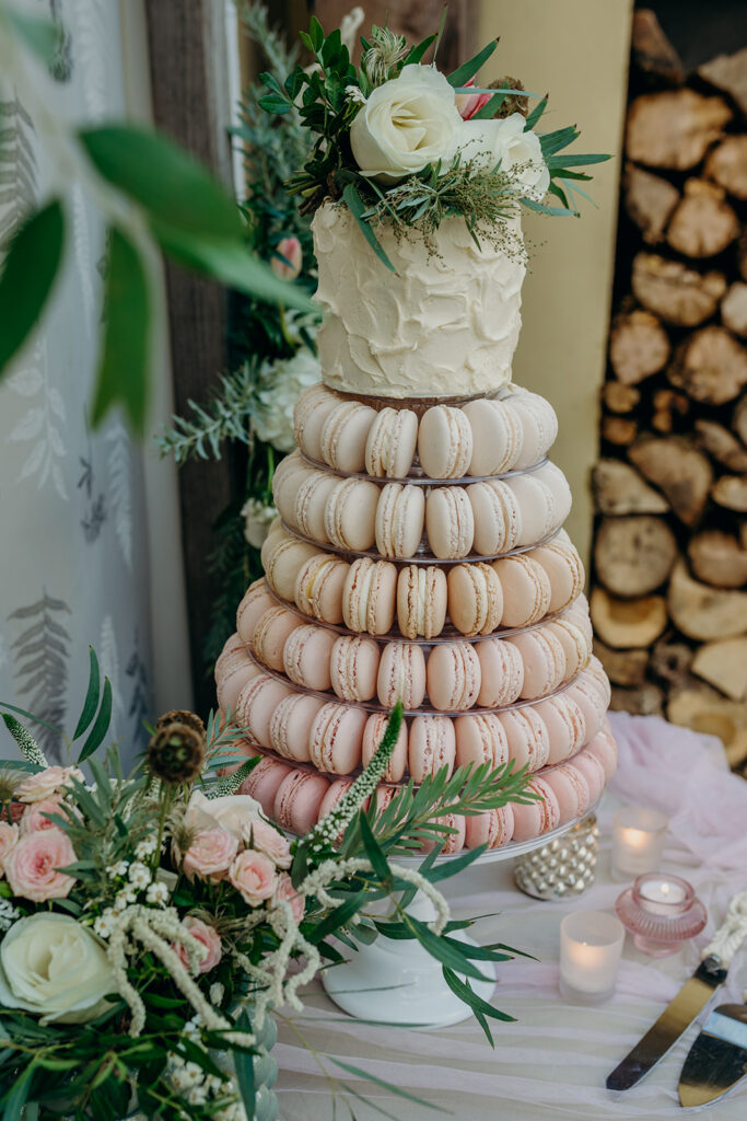 tight shot of ombre pink macaron tower on white cake stand topped with buttercream mini wedding cake dressed with fresh pink and white flowers