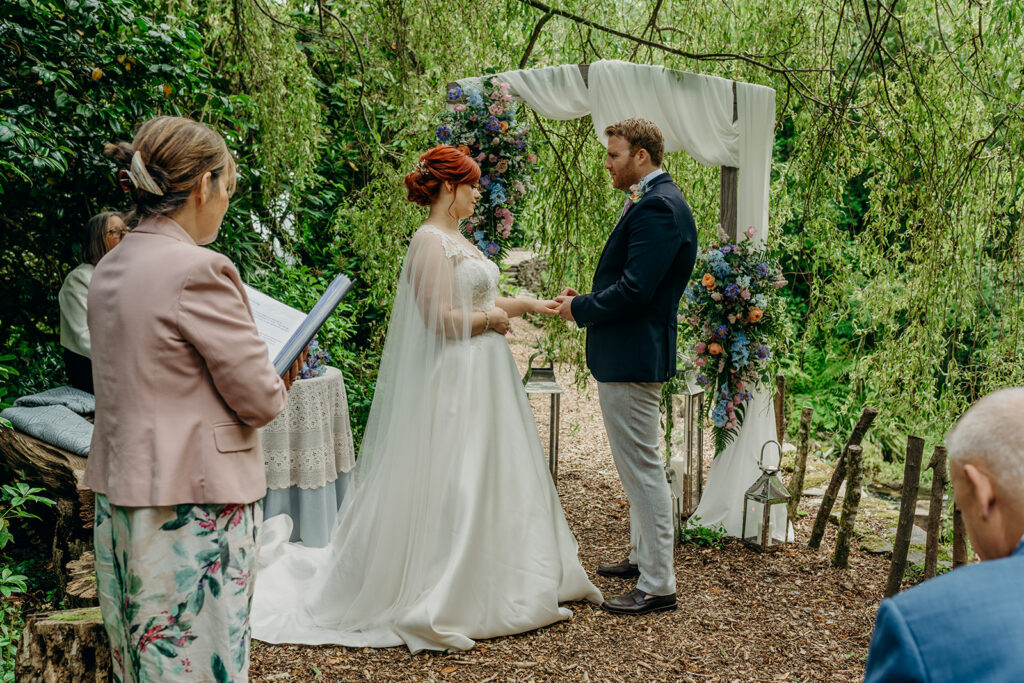 outdoor wedding ceremony under a willow tree with wedding arch and flowers