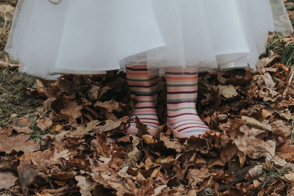 close up of bride and groom's daughter's wellington boots. They are pink and stripes and she stands in autumn leaves.