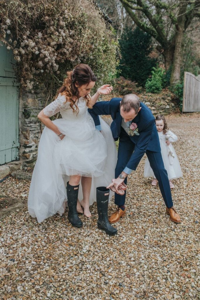 groom helping bride into her wellington boots with their daughter watching behind them