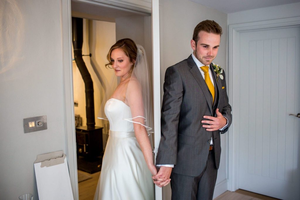 real wedding bride and groom first no-look behind a door holding hands